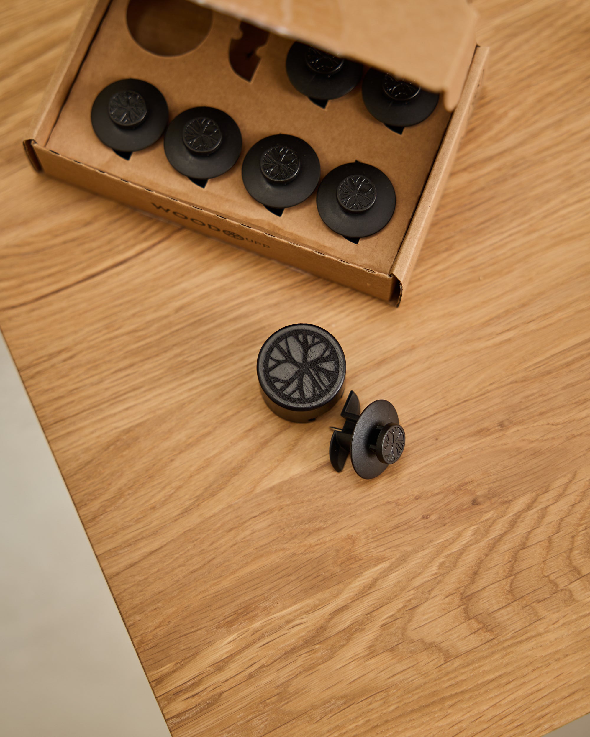 Black plastic fasteners are arranged on a wooden surface, with additional fasteners visible in an open cardboard box, used for installing acoustic panels.